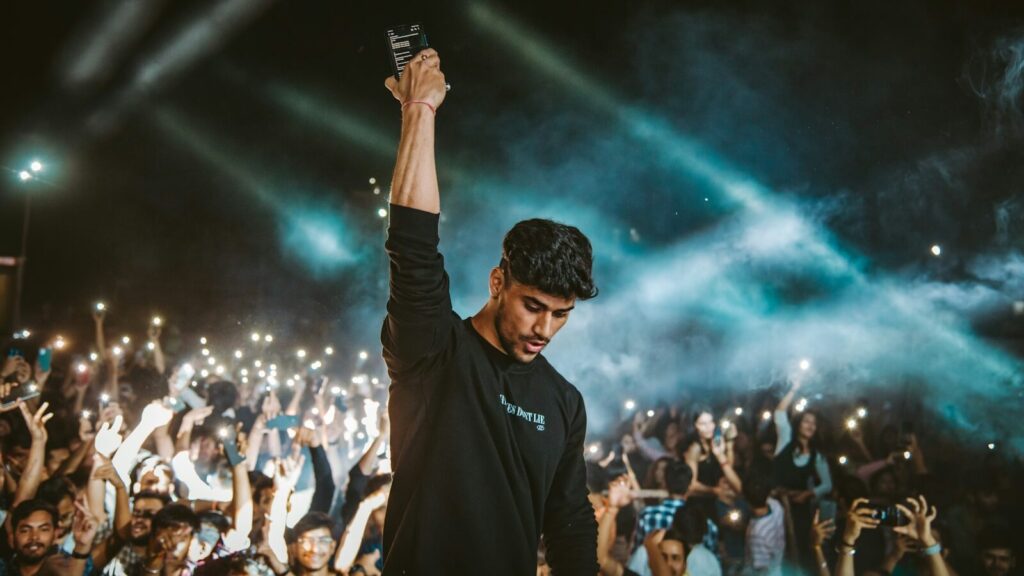 a man standing in front of a crowd holding a cell phone Master Your First DJ Gig
